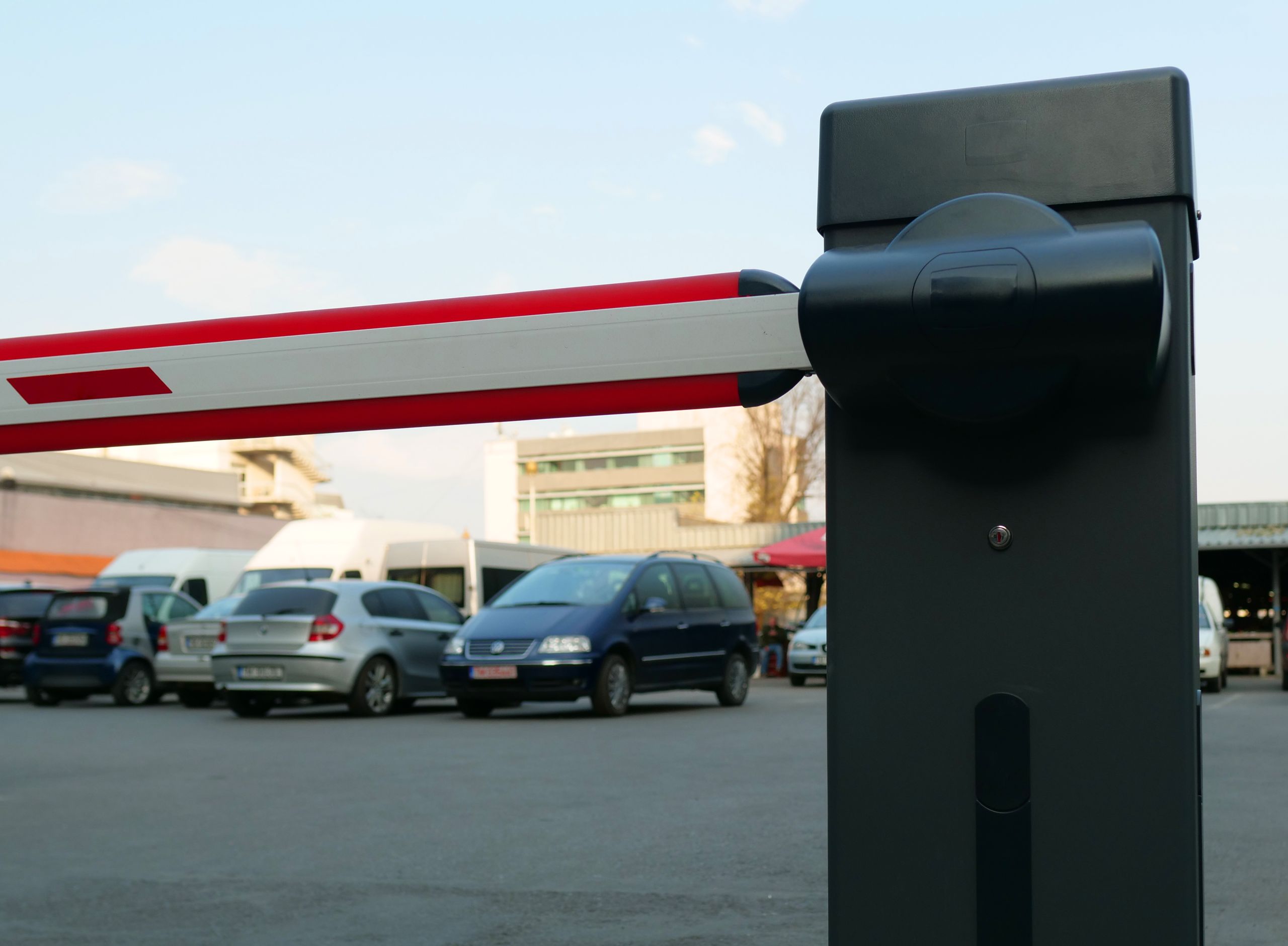Close-up of a parking lot barrier gate with vehicles in the background, modern and automated.