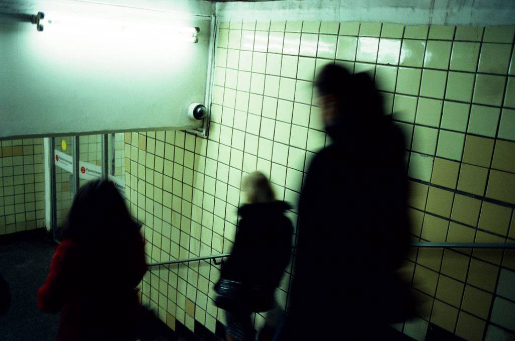 People walking down a tiled underground stairwell with motion blur effect, creating a dynamic scene.