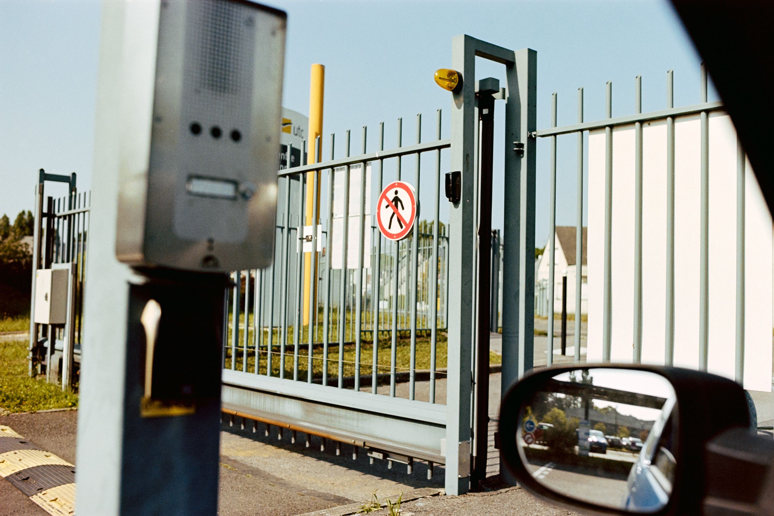 Security gate with no pedestrian sign and intercom, view from a car window.
