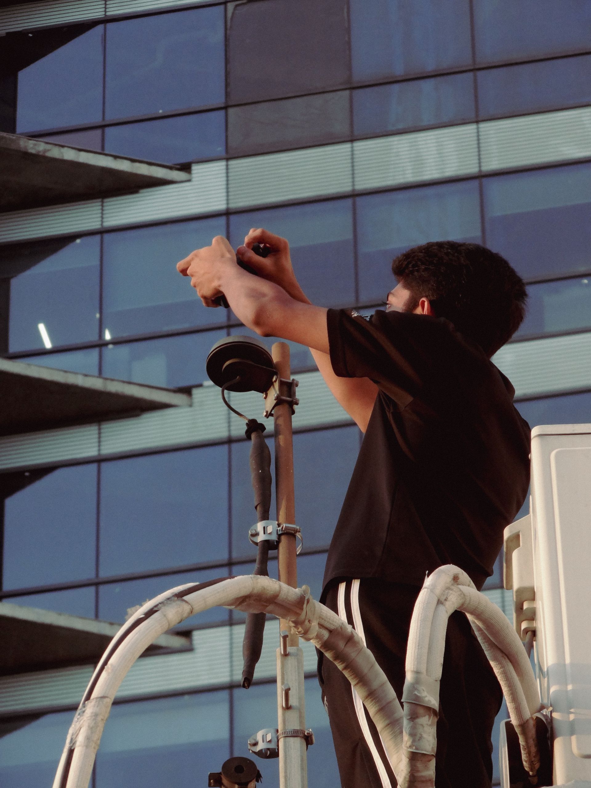 A man working with equipment on a rooftop against a modern urban building background.
