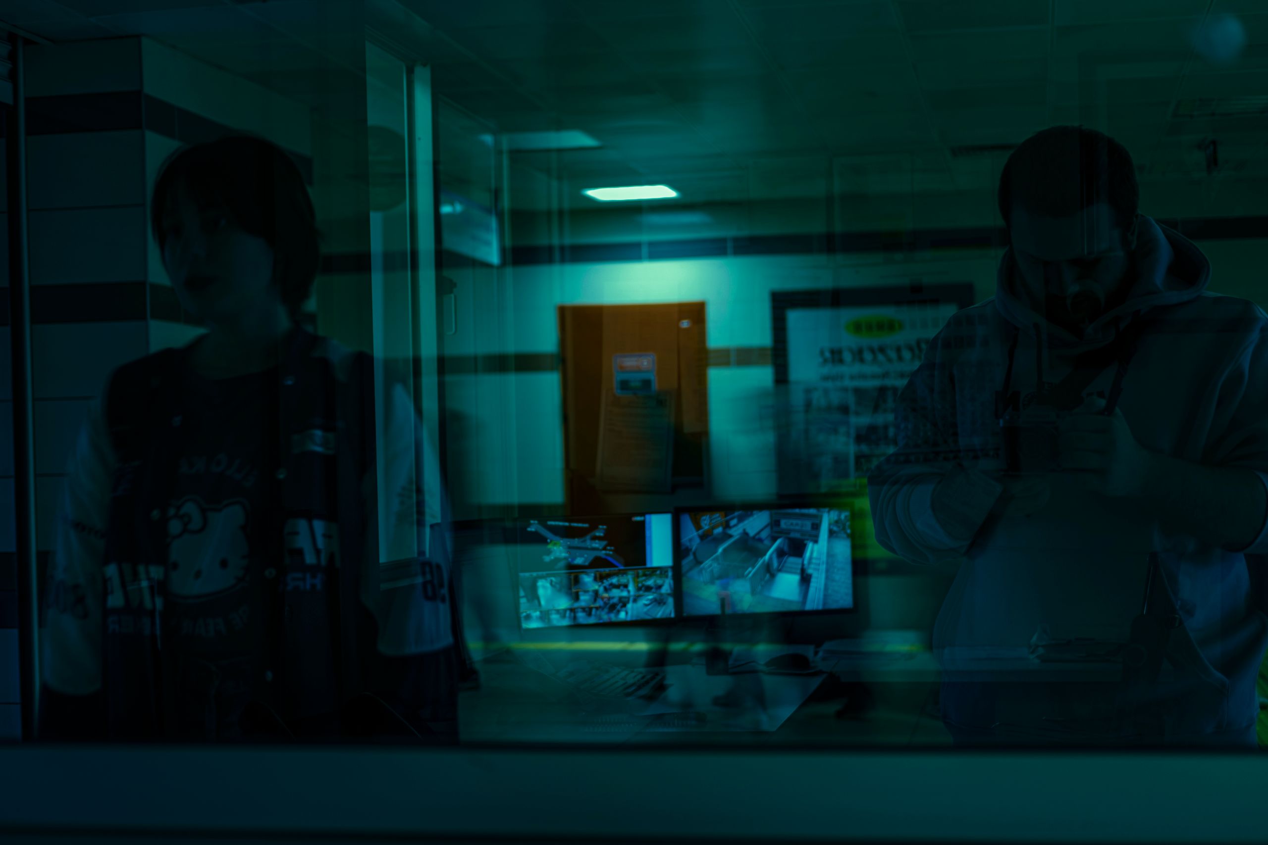 Shadowy figures reflected with security monitors in the foreground.